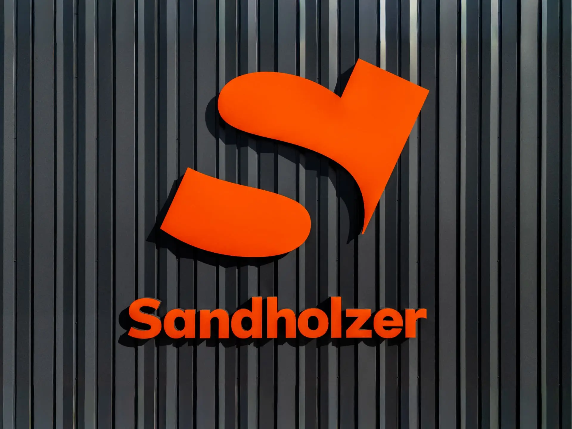 Orangefarbenes Sandholzer-Logo an der dunklen Fassade des Firmengebäudes